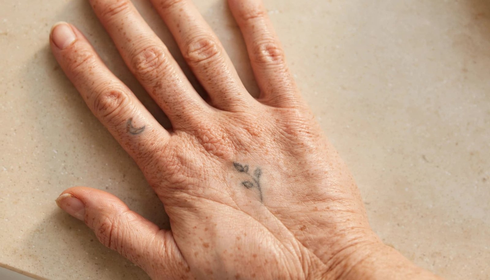 A single hand showing faded finger and palm tattoos in soft bathroom light.